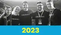 Grupo de cinco pessoas sorrindo, vestindo camisetas com o logo da empresa em um evento de 2023.